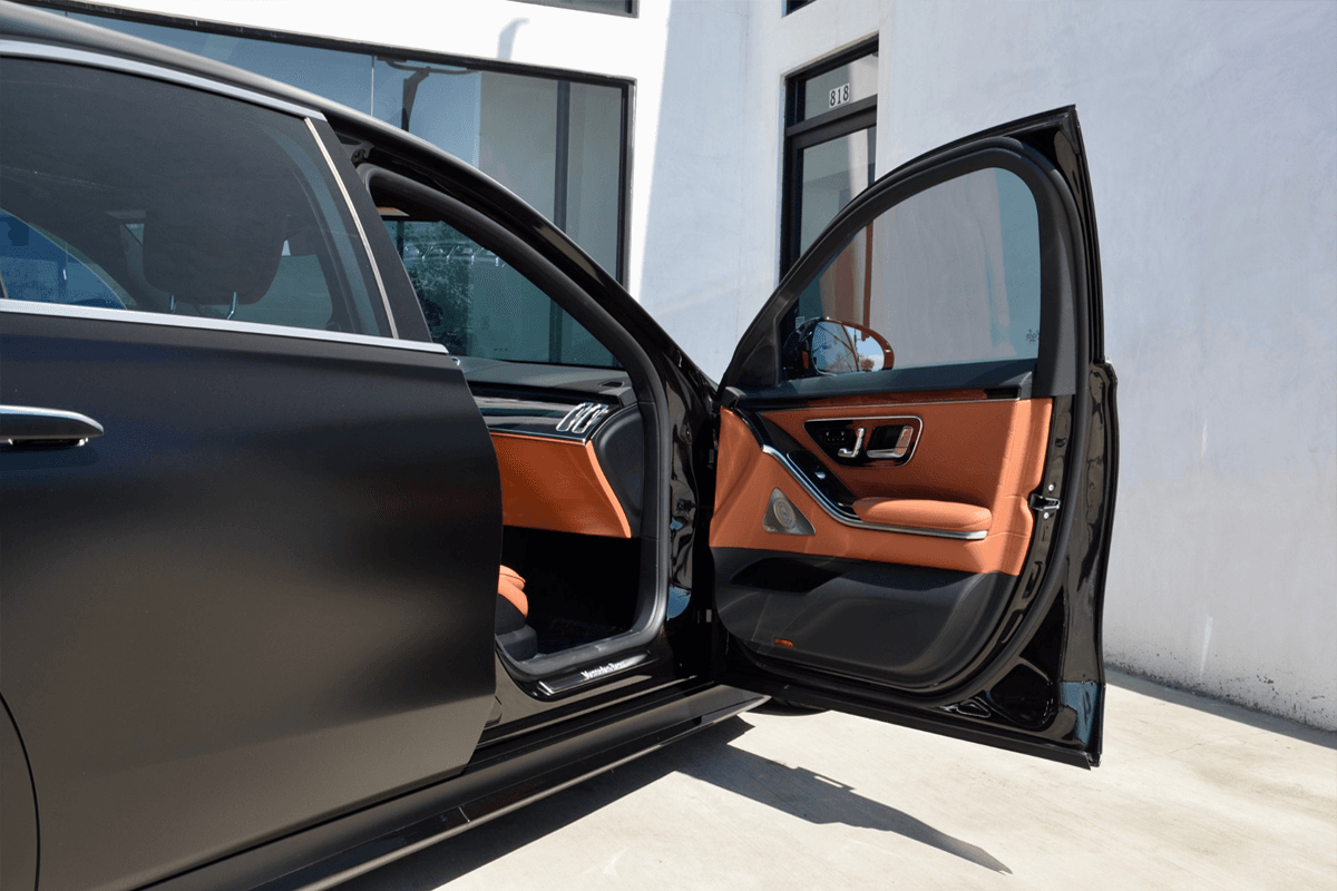A professional chauffeur opening the door of a black Mercedes-Benz S-Class S 580 for a business executive utilizing corporate transportation.