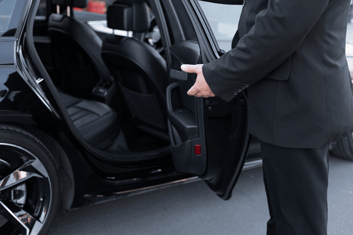 A professional driver opening the door of a luxury SUV for a client utilizing flexible hourly chauffeur service in the suburbs.