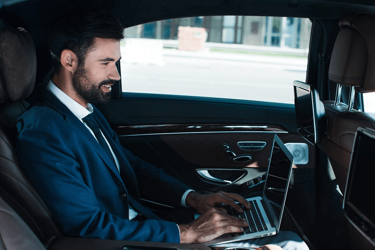 A business professional working on a laptop in the back of an ultra-luxury vehicle during an hourly chauffeur service booking.