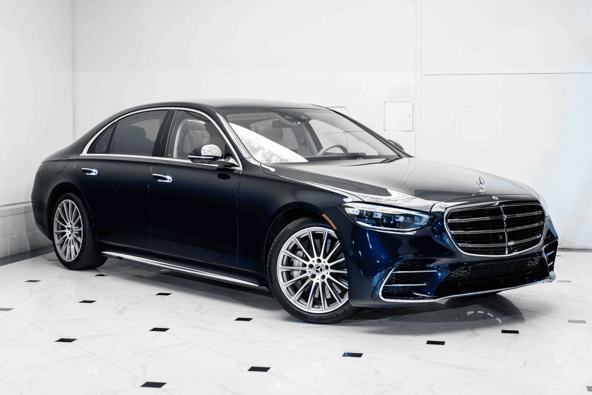 A professional chauffeur opening the door of a black Mercedes-Benz S-Class S 580 for a luxury airport transportation service pickup.