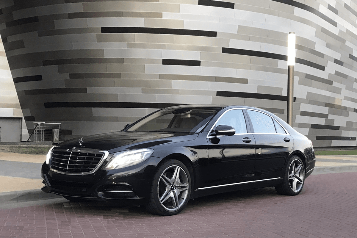 A black Mercedes-Benz sedan pulling up to a downtown Chicago hotel for a direct point-to-point car service drop-off.